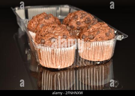 Mehrere leckere Schokoladen-Muffins in einem Plastikbehälter, Nahaufnahme, auf schwarzem Hintergrund. Stockfoto