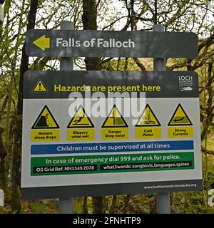 Schild mit Pfeil, der auf Fallfälle von Falloch in Schottland, Großbritannien, zeigt. Das Hotel liegt in der Nähe von Crianlarich in den schottischen Highlands. Schild warnt vor verschiedenen Gefahren Stockfoto