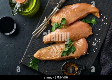 Rohes Hühnerfleischfilet, mariniert in Teriyaki-Sojasauce, Zwiebeln, Knoblauch und Pfeffer auf schwarzem Teller auf dunklem Schiefer, Stein oder Beton. Obere V Stockfoto