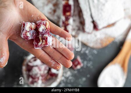 Eine Frau hält ein würfelförmiges Stück Obst und Nussgeschmack hausgemachten türkischen Delight mit Puderzucker bedeckt. Im Hintergrund in Stockfoto