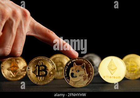 Symbolische Kryptowährungstypen, die als glänzende Münzen dargestellt werden, stehen vor dunklem Hintergrund. Unter ihnen ist Dogecoin, das als Witz begann, currentl Stockfoto