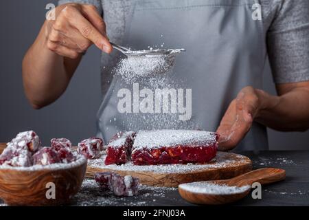 Herstellung von köstlichen Früchten aromatisierten hausgemachten türkischen Delight mit lebendigen rosa rote Farbe und gemischt mit Haselnüssen. Gesiebte Konditoren Zucker wird hinzugefügt Stockfoto