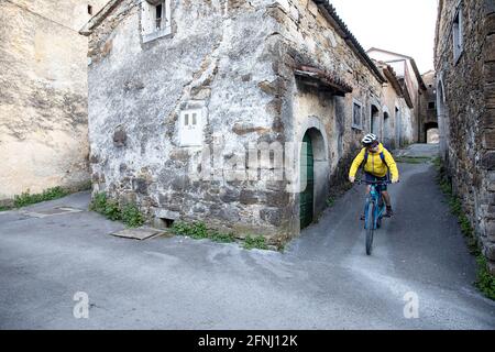 Junge Radfahren in der engen Straße von Goce, kleines Dorf im Vipava-Tal, slowenische Landschaft, vorbei an rustikalen traditionellen Steinhäusern, Stockfoto