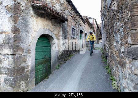 Junge Radfahren in der engen Straße von Goce, kleines Dorf im Vipava-Tal, slowenische Landschaft, vorbei an rustikalen traditionellen Steinhäusern, Stockfoto