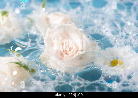 Weiße Rose auf Blasen Badeschaum. Spa, Bio-Hygieneprodukte, Kosmetik, andere Toilettenartikel Konzept. Stockfoto