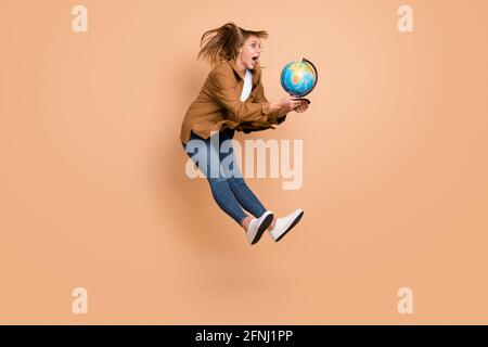 Full-Size-Profil Seite Foto von jungen überrascht Mädchen überrascht Springen fangen Erdkugel isoliert auf beigefarbenen Hintergrund Stockfoto
