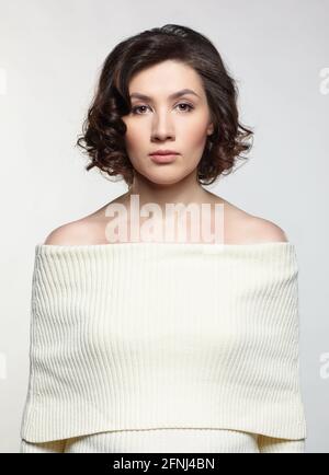 Brunette schöne Frau in großen weißen Wollpullover auf grauem Hintergrund gekleidet. Stockfoto