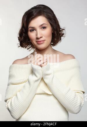 Brunette schöne Frau in großen weißen Wollpullover auf grauem Hintergrund gekleidet. Weibchen mit verschlammten Händen. Stockfoto