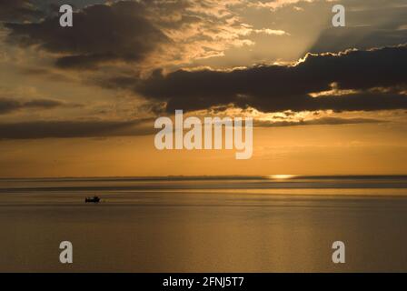 Ein Bild eines perfekten Sonnenuntergangs entlang der Küste von Norfolk mit dem goldenen Glanz des frühen Abends und einem Fischerboot in Silhouette auf einem ruhigen und friedlichen Meer Stockfoto