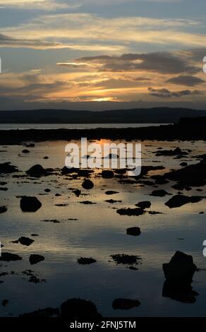 Sonnenuntergangsbild entlang der Küste von Northumbria mit Licht am Himmel und einem goldenen Glanz auf einem ruhigen Meer mit zahlreichen Felsen in Silhouette gegen die Farbe Stockfoto