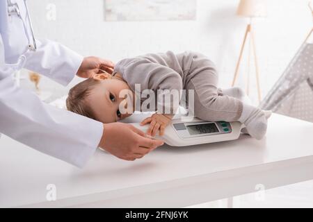 afroamerikanischer Kinderarzt, der den Kleinkind auf der Babywaage unterstützt Stockfoto