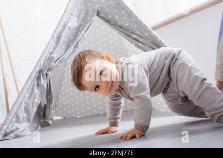 Kleiner Junge im Strampler, der zu Hause in der Nähe von Tipi kriecht Stockfoto