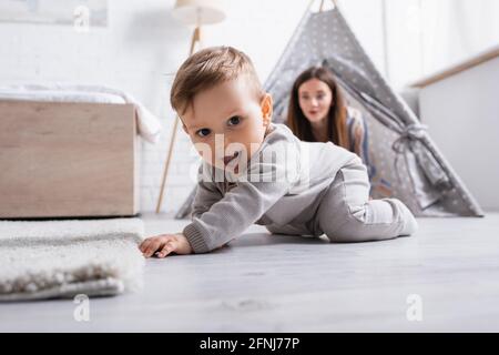 Aufgeregt Baby Junge kriechen auf dem Boden in der Nähe der Mutter auf verschwommen Hintergrund Stockfoto