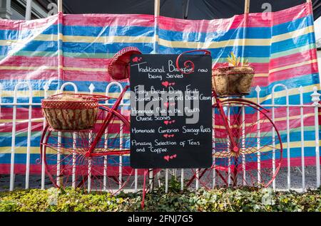 Die Speisekarte des Restaurants Poppi Red steht auf einer Tafel, die an einen rot gestrichenen Zyklus in Hawkshead, Cumbria, England, angeschlossen ist Stockfoto