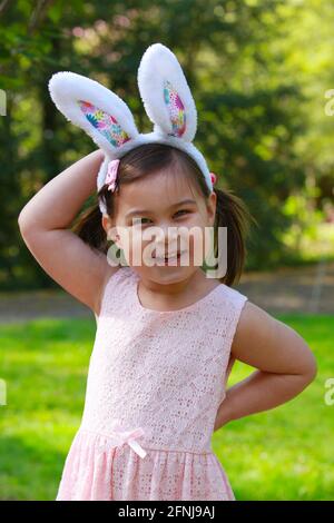 Kleines Mädchen auf dem Rasen trägt ein rosa Kleid und Hasen Ohren an Ostern. Stockfoto