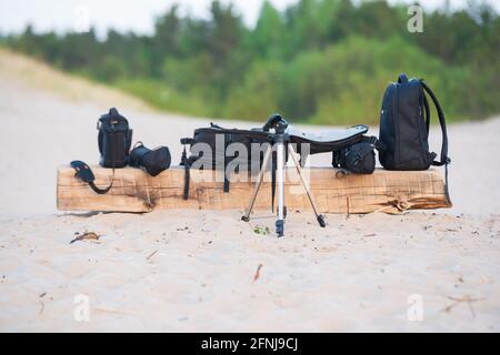 Fotoausrüstung - Fototasche, Stand am Meer in den Dünensand auf einer hölzernen Brettbank. Stockfoto