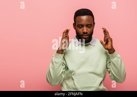 afroamerikanischer Mann mit gekreuzten Fingern isoliert auf rosa Stockfoto