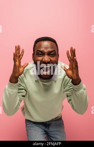 Wütender afroamerikanischer Mann, der die Kamera isoliert auf Pink anschreit Stockfoto