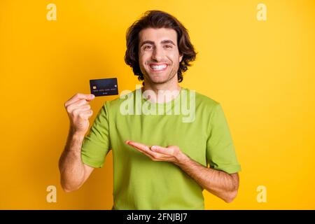 Portraitfoto des lächelnden fröhlichen Mannes, der die Kreditkarte der Bank hält Lächelnd isoliert auf hellgelbem Hintergrund Stockfoto