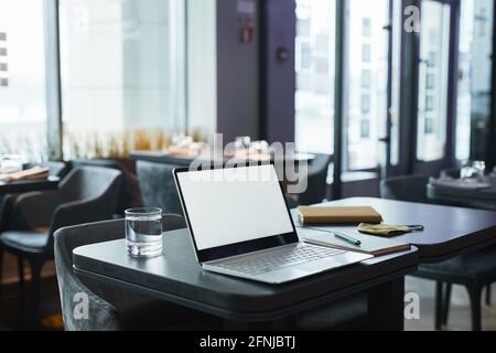 Moderner Laptop mit weißem Bildschirm, Glas Wasser und Organisator mit Stift auf dem Tisch im Café, Freiberufler Arbeitsplatzkonzept Stockfoto