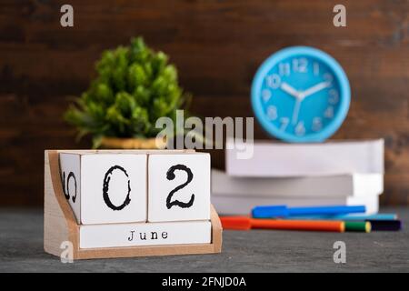 Juni. Juni 02 Holzwürfelkalender mit unscharfen Objekten auf dem Hintergrund. Stockfoto