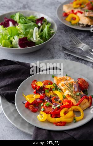 Gebackenes rotes Fischfilet Arctic Saibling auf einem Teller mit Gemüse, Salat in einer Schüssel mischen, leckeres herzhaftes gesundes Abendessen Stockfoto