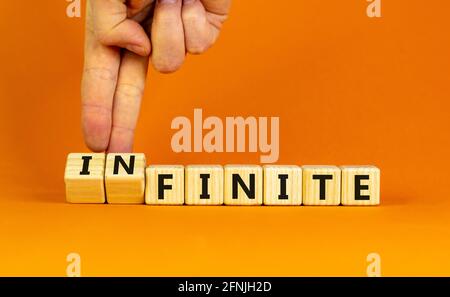 Endliches oder unendliches Symbol. Geschäftsmann dreht Holzwürfel und ändert das Wort 'endlich' in 'unendlich'. Schöner orangefarbener Tisch, orangefarbener Hintergrund. Busi Stockfoto