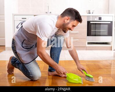 Hübscher Mann, der den Boden fegen und vor dem eine Schutzumpfanne steht Küchenschränke zu Hause Stockfoto