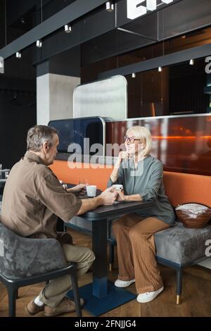 Schöne reife Frau mit blonden Haaren sitzt am Tisch und Dem Freund beim Date im Restaurant zuhören Stockfoto