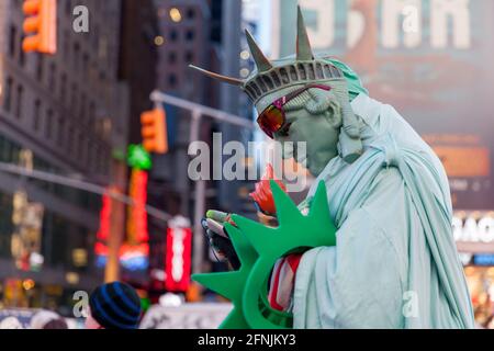 Mann in einem Kostüm der Freiheitsstatue beim Überprüfen des Mobiltelefons Stockfoto