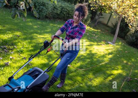 Hübsche junge Frau mäht Rasen im Hinterhof Stockfoto