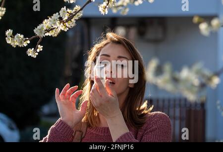 Hübsche junge Frau, die im Frühling vor einem blühenden Baum eine Asthmapumpe benutzt. Saisonaler Allergieanfall Stockfoto