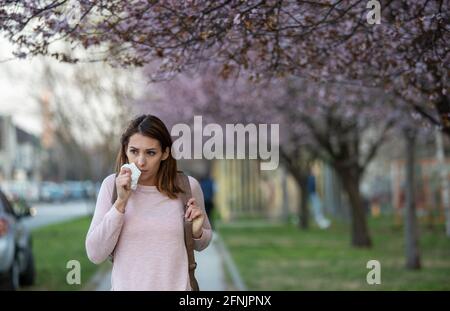 Hübsches junges Mädchen, das in der Straße unter blühendem Baum läuft Frühling und allergische Reaktion auf Pollen der laufenden Nase Stockfoto