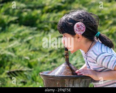 Bukarest, Rumänien - 04.10.2021: Durstiges junges Mädchen, das Wasser aus einem Wasserhahn oder Brunnen im Park trinkt. Stockfoto