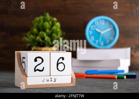 Juli. Juli 26 Holzwürfelkalender mit unscharfen Objekten auf dem Hintergrund. Stockfoto