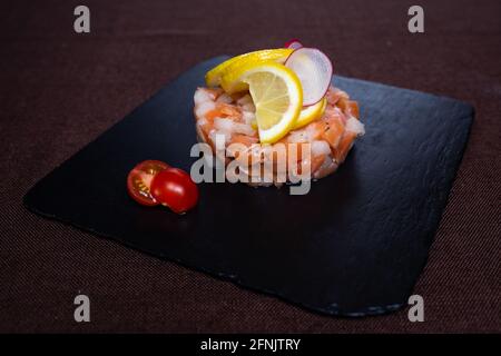 Gericht im Restaurant von rotem Fisch mit Zitrone auf Eine schwarze Platte Stockfoto