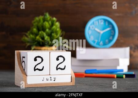 Juli. Juli 22 Holzwürfelkalender mit unscharfen Objekten auf dem Hintergrund. Stockfoto