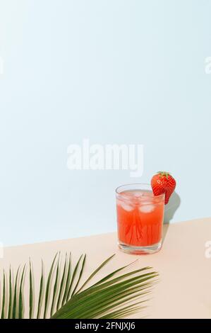 Ein fruchtiger Erdbeer-Erfrischungsgetränk mit Eis. Tropisches Palmenblatt verschwommen vor dem Glas. Party Sommer erfrischendes Konzept auf einer Kombination aus b Stockfoto