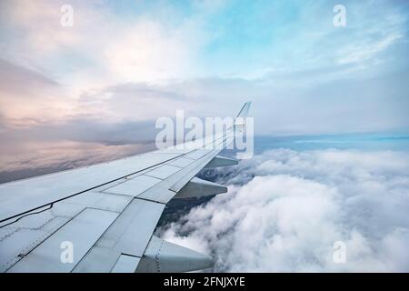 Blick auf den Flugzeugflügel im Flug über Wolken mit Sonnenuntergang Stockfoto