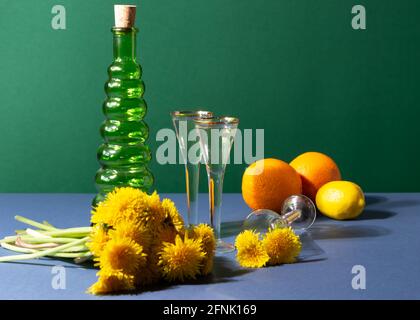 Dandelion Wein in Jahrgangswinzern. Modernes Stillleben mit Zutaten für die Zubereitung Kräutermischung. Grüne Flasche, zwei Orangen, Limette und Bouquet Stockfoto