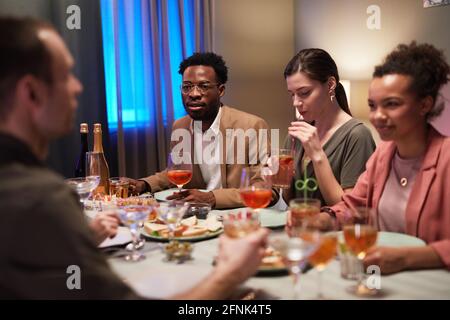 Eine Gruppe junger Leute, die beim Abendessen am Tisch sitzen Feiern Sie drinnen Stockfoto