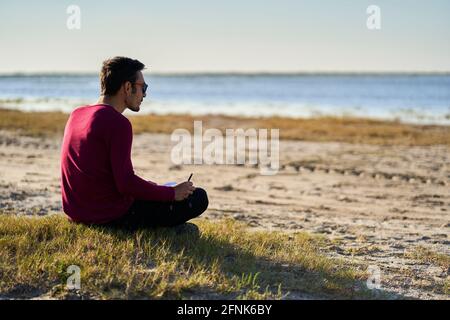 Junger Mann, der am Strand schreibt Stockfoto