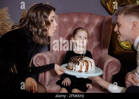 Kleines Mädchen bläst die Kerzen auf dem Kuchen mit Ihre Eltern Stockfoto