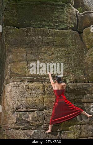 Frau Bouldern auf den Sandsteinfelsen in rotem Kleid Stockfoto