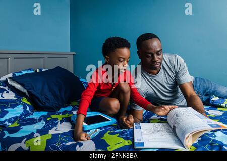 Vater, der Sohn beim Studieren im Schlafzimmer zu Hause unterstützt Stockfoto