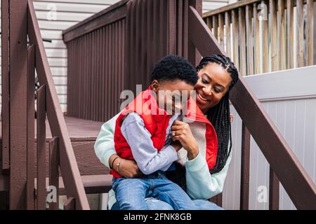 Fröhliche Mutter und Sohn sitzen auf einer Treppe im Hinterhof Stockfoto