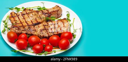 Zwei gegrillte Schweinesteaks auf einem Teller mit gekeimtem Kichererbsen und Tomaten auf türkisfarbenem Hintergrund. Stockfoto
