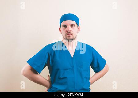 Junger Arzt Porträt mit Händen auf den Hüften in blauen Chirurgen Anzug und schützende Atemmaske auf gelbem Hintergrund isoliert Stockfoto