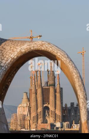 Blick auf die Basílica de la Sagrada Família durch den Bogen von Antoni Gaudí Stil Kamin auf dem Dach von La Pedrera, Barcelona, Spanien Stockfoto