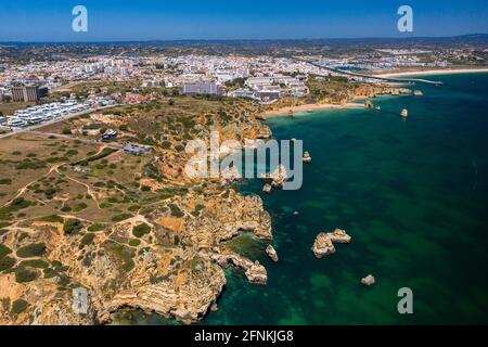 'Ponta da Piedade' - portugiesische goldene Küstenklippen im Süden. Luftaufnahme über die Stadt Lagos an der Algarve, Portugal. Im Hintergrund der Strand Meia praia. Stockfoto